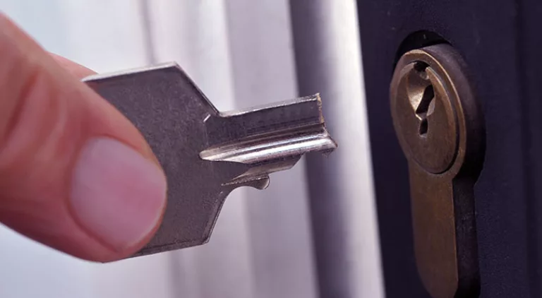 Afgebroken sleutel naast een cilinderslot in een zwarte deur